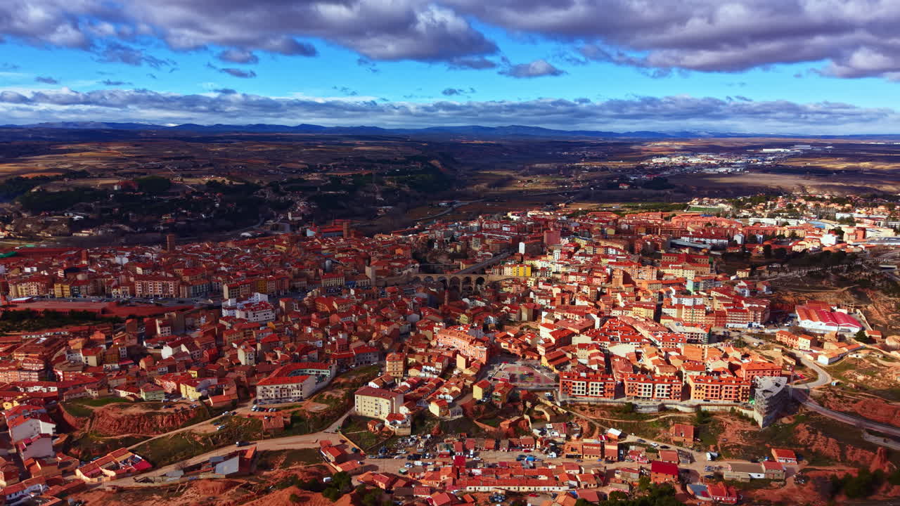 Vista di una città con tetti rossi sotto un cielo nuvoloso, in una zona montuosa di giorno.