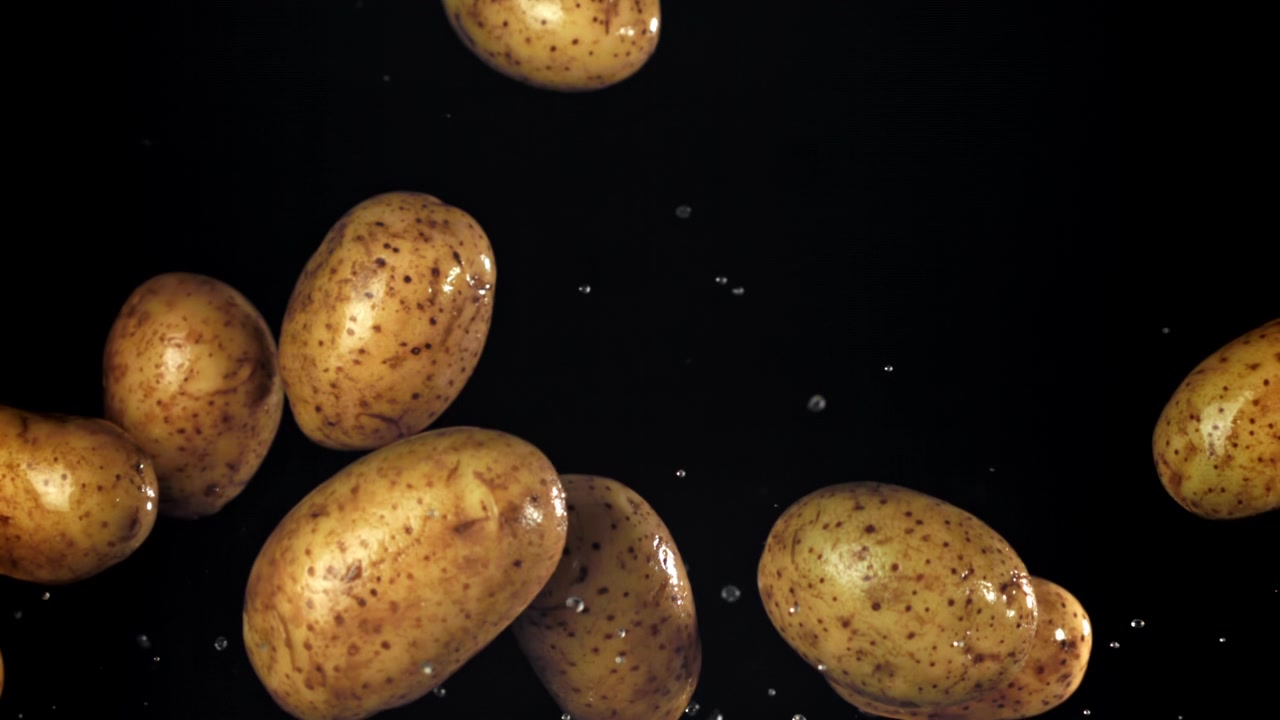 Patate fresche con goccioline d'acqua che cadono a rallentatore su sfondo nero