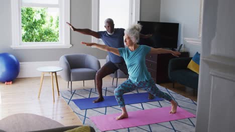 Mixed-race-senior-couple-performing-exercise-together-in-the-living-room-at-home