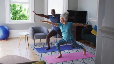 mixed race senior couple performing exercise together in the living room at home