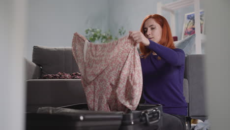 excited woman puts summer dresses into big open suitcase