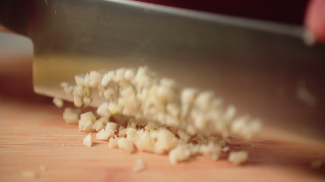 Mincing garlic by hand with a knife on a cutting board