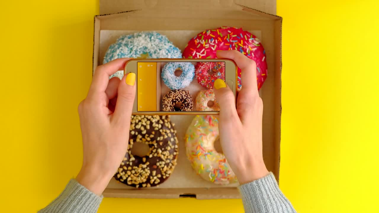 las manos de la mujer toman fotos con el teléfono inteligente de deliciosas rosquillas en la caja