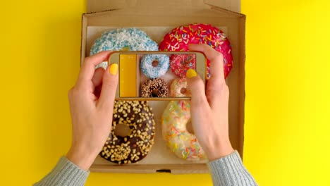 woman's hands take pictures with smartphone of delicious donuts in box