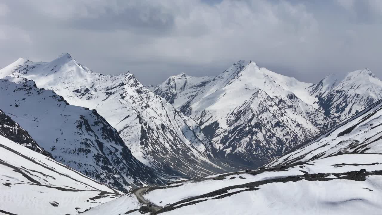 Aerial drone shot of Shinkula Pass highlighting towering mountains cloaked in thick snow.