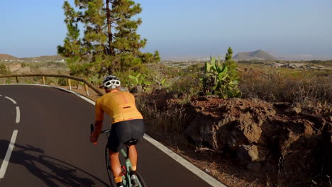 In-Diesem-Video-Verfolgt-Die-Kamera-Die-Fahrt-Eines-Männlichen-Radfahrers-Eine-Bergstraße-Hinauf.-An-Einem-Sonnigen-Tag-Absolviert-Er-Ein-Radtraining-Auf-Einer-Hügeligen-Autobahnstraße