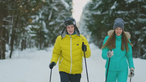 portrait of a married couple. a man in a yellow jacket and a woman in a blue jumpsuit in the winter in the woods skiing in slow motion