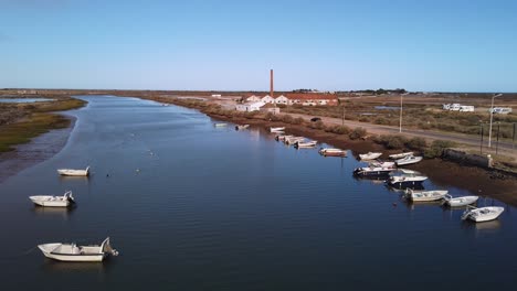 Boats-tied-off-along-Gilao-River-bank-at-low-tide-as-sun-sets,-Tavira,-Portugal,-wide