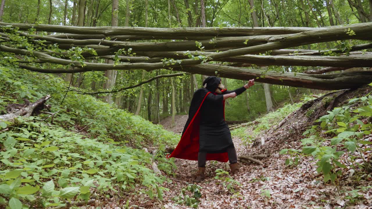 parca en capa negra con capucha bailando en el bosque bajo el tronco de un árbol caído