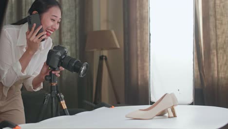 asian female photographer talking on smartphone while taking photos of women's shoes in home studio