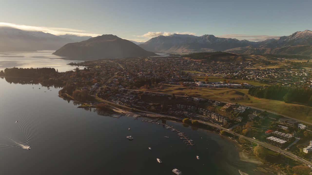 Ampia inquadratura aerea di un drone della città di Wanaka con lago e barche al tramonto. Tranquilla città in Nuova Zelanda. Catena montuosa e nuvole in lontananza.