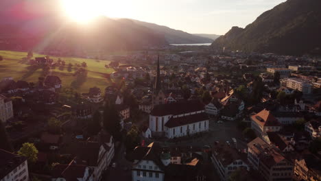 Orbiting-around-the-city-of-Lucern-at-sunet,-showing-the-skyline-and-churches-with-towering-mountains