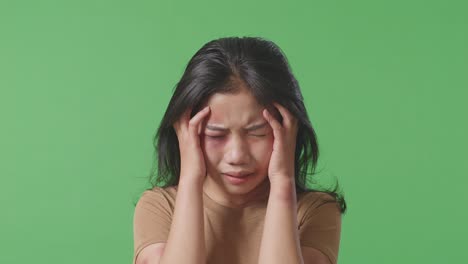 close up of young asian woman victim of violence with bruise on face having nervous breakdown and screaming in the green screen background studio