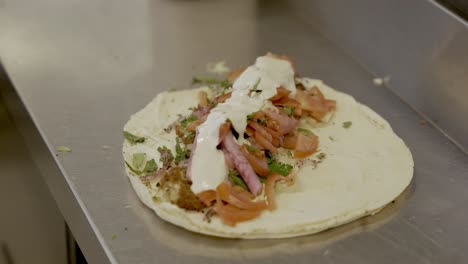 chef in restaurant's kitchen adding mayonnaise and sauce over chicken shawarma