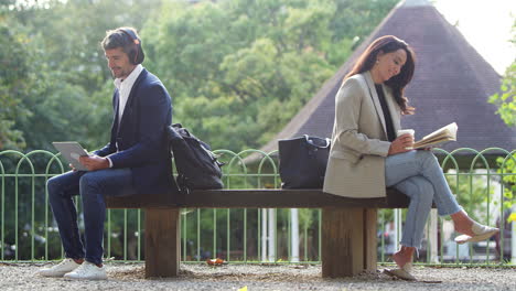 businessman and businesswoman on a break outdoors reading book and watching digital tablet