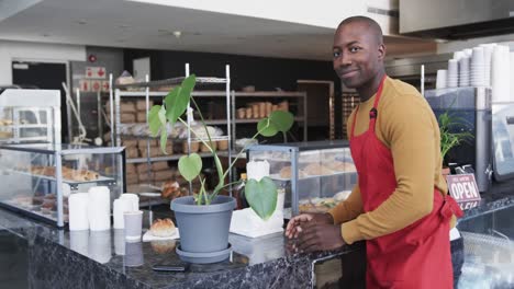 portrait of happy african american male worker with arms crossed in bakery in slow motion