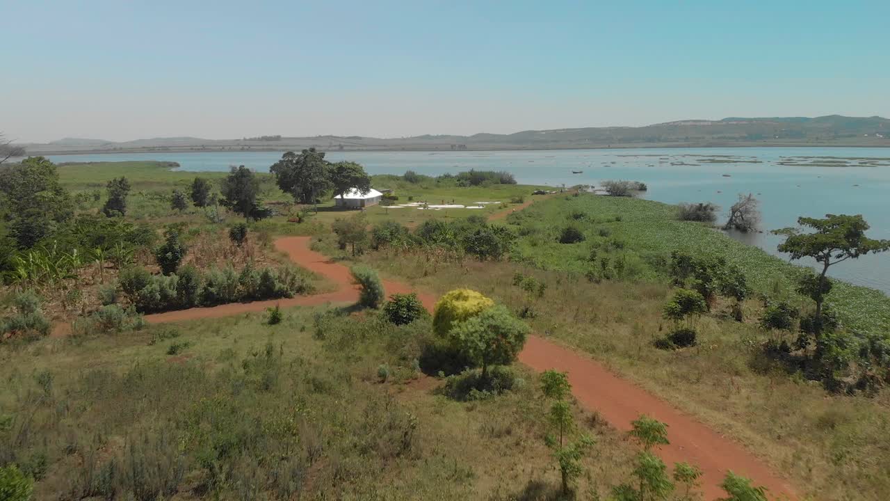 Ripresa aerea che segue un'auto su una strada sterrata polverosa lungo le rive del Lago Vittoria nell'Africa rurale