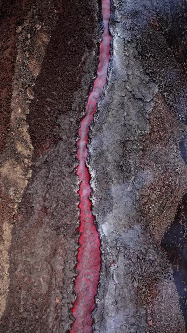 Lave en fusion serpentant sur un terrain volcanique avec de la fumée s'élevant, vue d'en haut