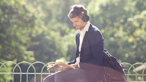 hombre de negocios leyendo un libro y escuchando en auriculares en el parque con café para llevar