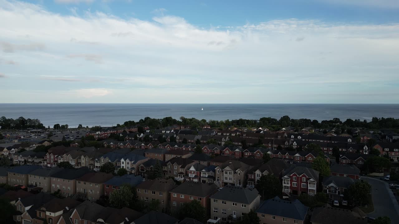 Drone view of suburban homes and tree-lined streets in Pickering, Ontario, with Lake Ontario on the horizon and evening light casting soft shadows over the peaceful neighborhood