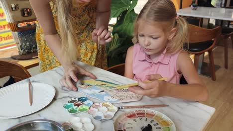 mother and daughter painting a ceramic plate in a cafe