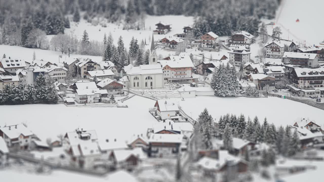 A snow-covered Tyrolean village with alpine houses and hotels at the foot of the skiing slope nestled in the Dolomites.