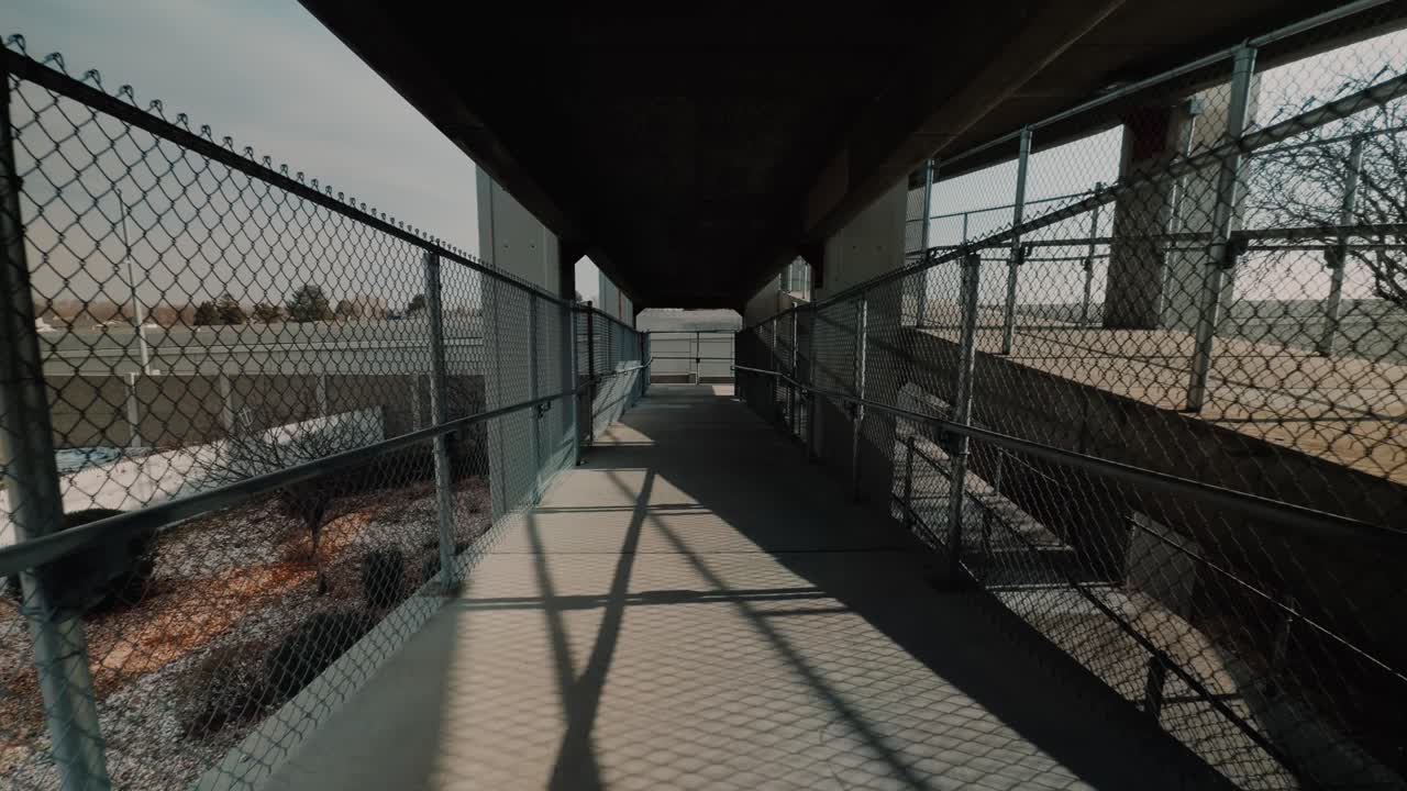Szerokokątne ujęcie z panoramowaniem w ruchu przez ogrodzone przejście dla pieszych pod wiaduktem.