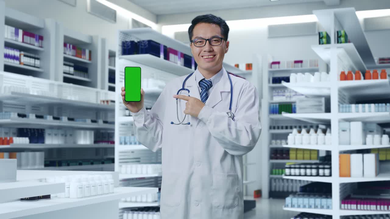 약국 에 서 있는 동안 손 에 초록색 스크린 의 스마트폰 을 가리키는 스테토스코프 를 들고 있는 아시아 남자 의사