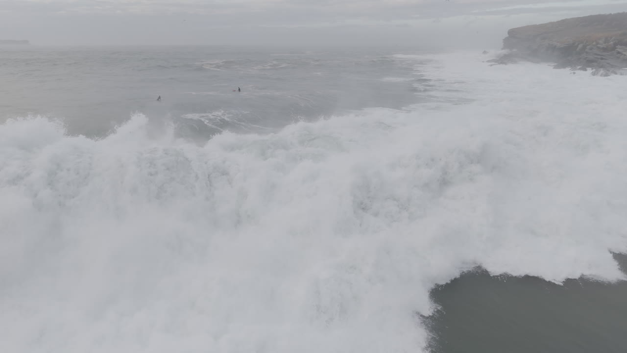 Surfer Riding a Massive Ocean Wave Near a Rocky Coastline