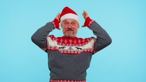 man wears red new year deer sweater raising hands in surprise shocked by sudden victory, wow emotion
