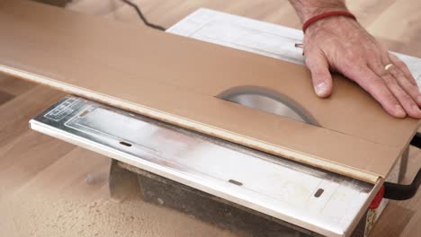 cutting laminate floor boards on circular saw, detail on man hand holding the panel