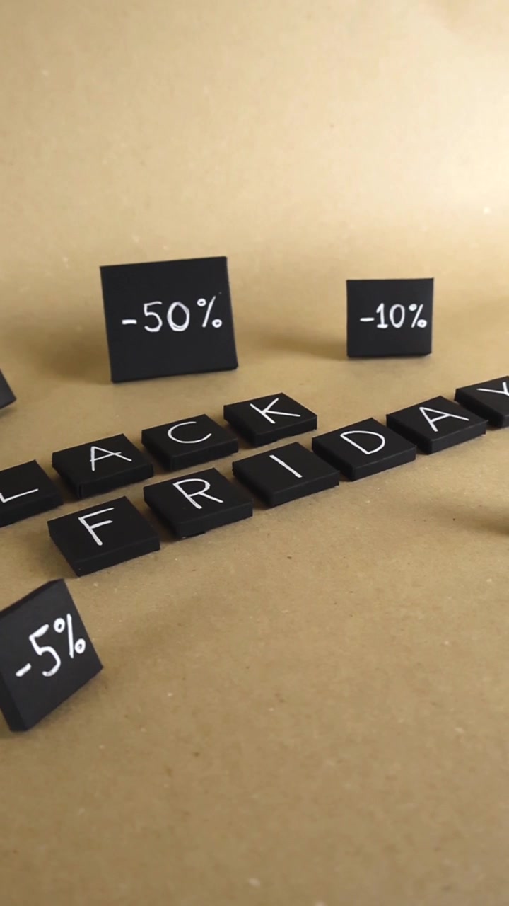 Handmade black paper tiles showing the text Black Friday and different discount percentages gliding on a light brown background, representing the best time for consumerism and shopping