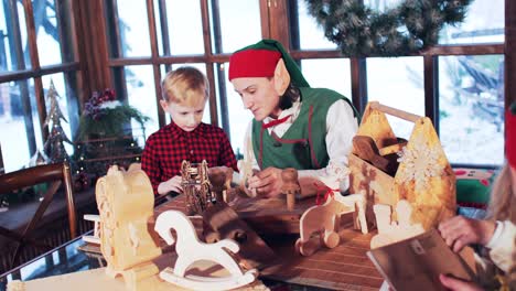 a boy in a red shirt is played with wooden toys with a christmas elf in the residence of santa claus