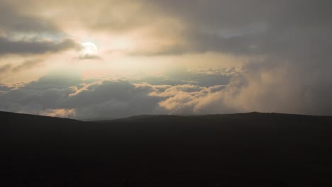 sunlight piercing through dramatic clouds over dark hills