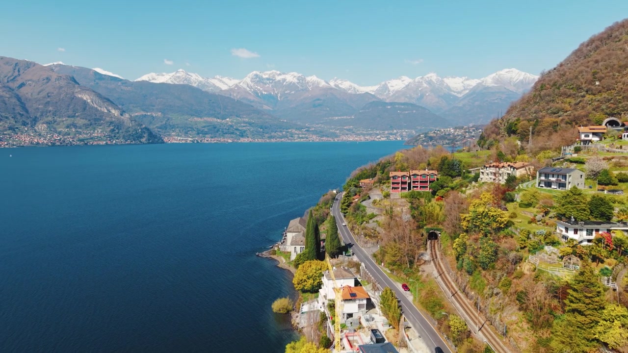 Vista dall'alto della panoramica strada del Lago di Como, auto, vetta alpina innevata.