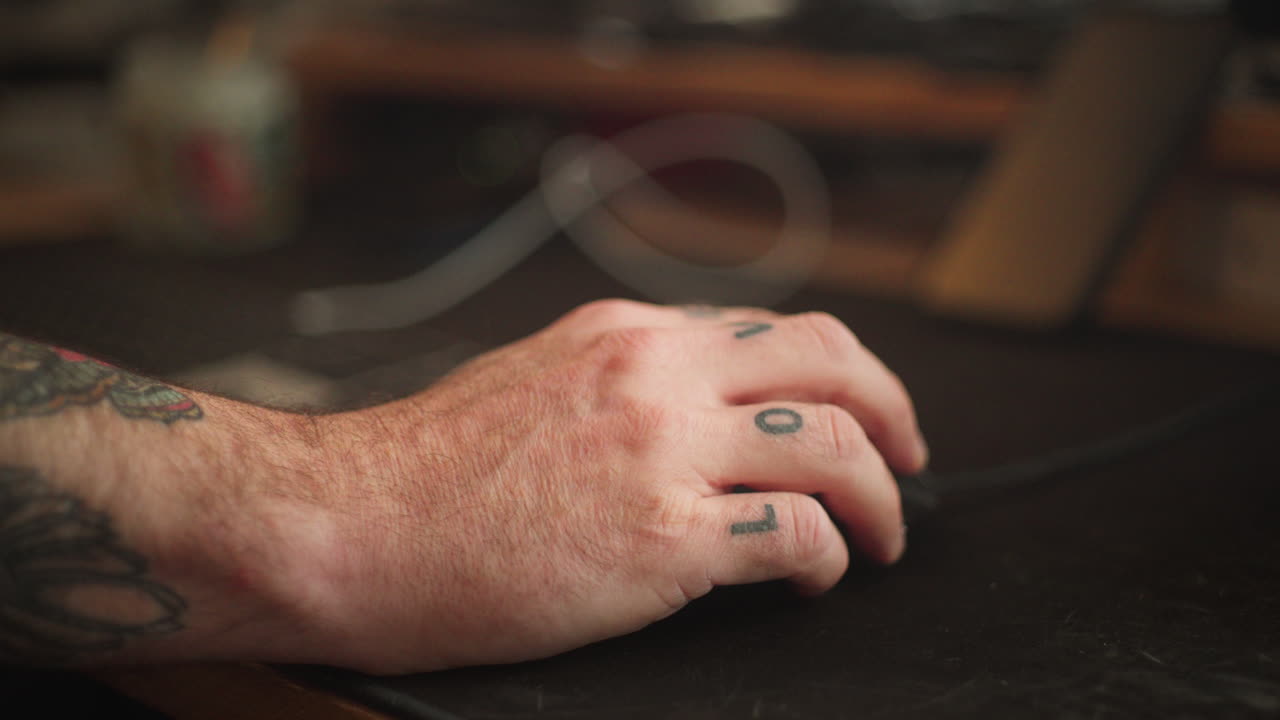 A close-up of a tattooed hand using a computer mouse, highlighting the detailed tattoos on the fingers