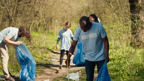 African-american-man-volunteer-collecting-trash-and-plastic-waste-with-tongs