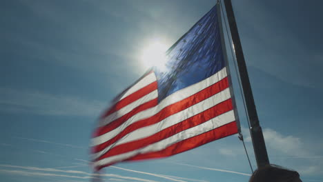 united states flag flapping powerfully in the wind as the sun creates a flare behind it