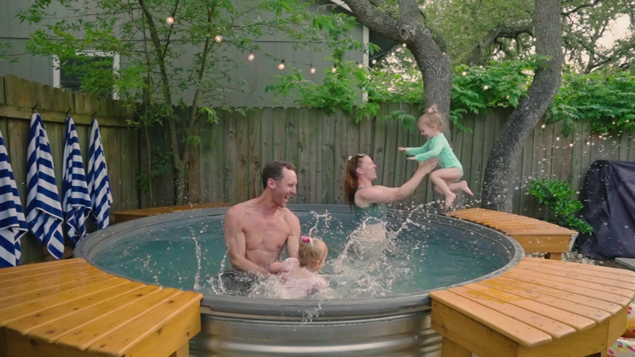Famiglia che sguazza in una piscina stocktank in giardino, il papà solleva uno dei gemelli e la mamma tiene l'altro, mentre tutti e quattro ridono e giocano. Perfetto per annunci di lifestyle familiare, divertimento estivo e contenuti per giornate in piscina