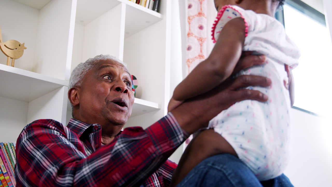 Grandfather Lifting Baby Granddaughter Into The Air And Smiling At Home