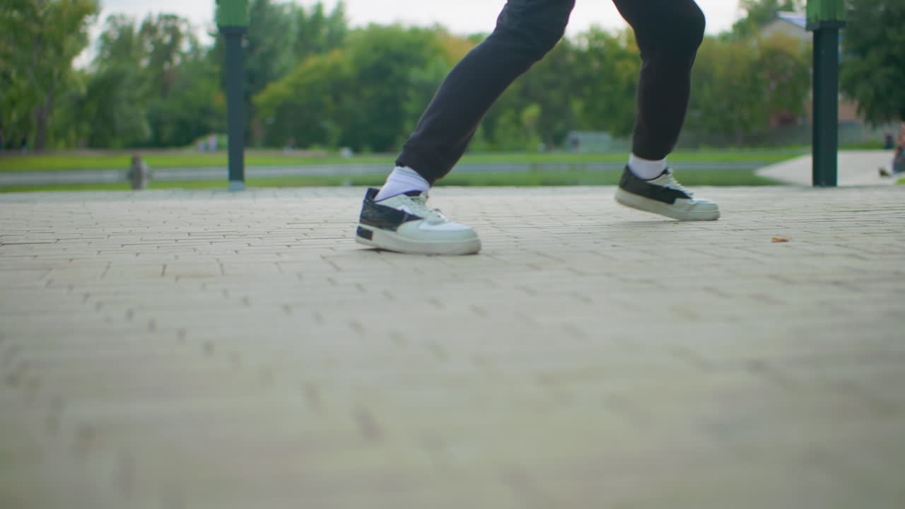 park pavement duet street dance session two dancers exchanging steps on open plaza near trees and benches white and black sneakers sync exercises playful sparring community park setting natural light