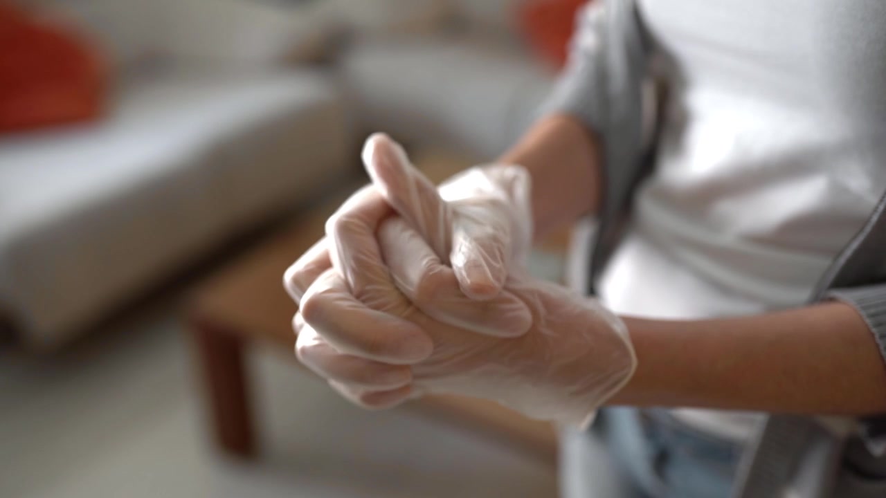 Mujer poniéndose guantes en casa durante la cuarentena por COVID-19