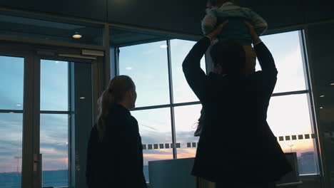 young family looking out airport window at sunset