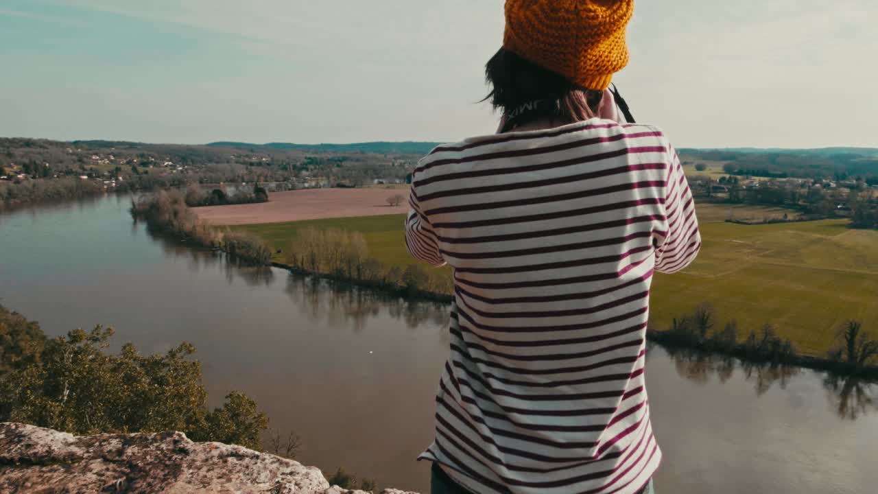 Close-up circular tracking shot of a woman on the edge of a cliff, she takes pictures of the landscape
