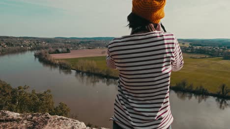 close-up circular tracking shot of a woman on the edge of a cliff, she takes pictures of the landscape