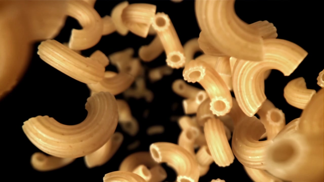 Pasta maccheroni secca che cade al rallentatore su sfondo nero.