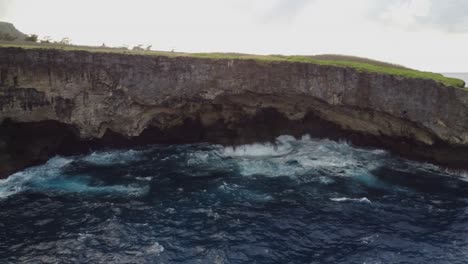 Schwenk-Einer-Klippe-Mit-Wellen,-Die-Auf-Felsen-Krachen,-Drohnenaufnahme