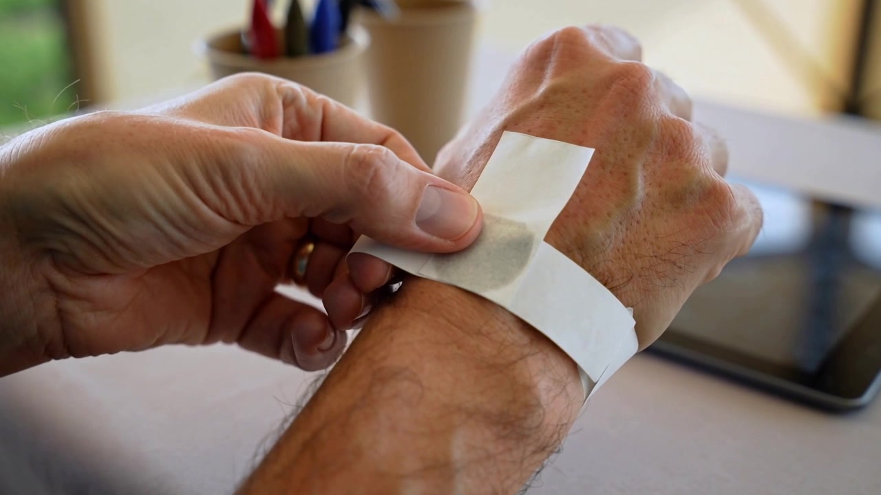 Rimozione del supporto, mani e braccio nudo che allineano, premono e lisciando il cuscinetto su una striscia di carta a casa per fissarlo