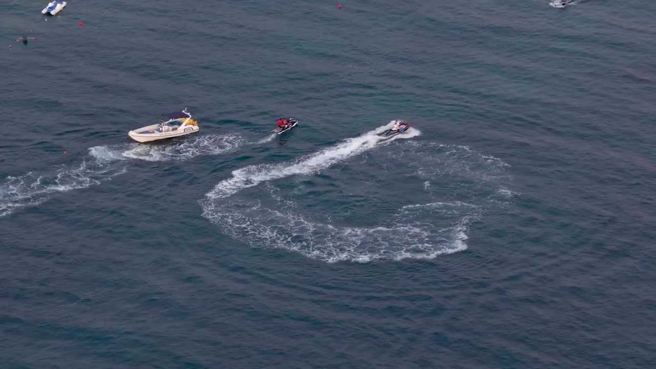 Pemandangan udara drone dari perahu cepat dan jet ski yang melaju kencang di perairan laut lepas, menciptakan ombak busa putih, aktivitas olahraga musim panas di Ksamil Albania