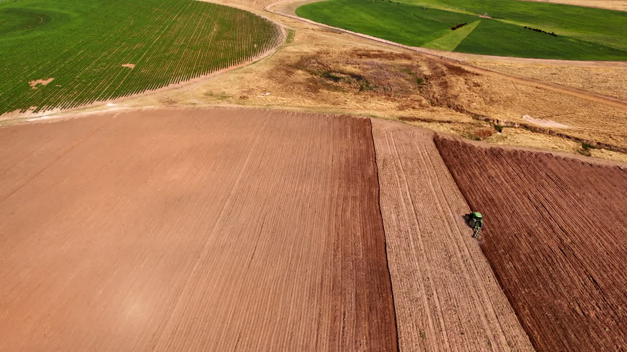 High angle drone view over arable brown farm land being ploughed by tractor
